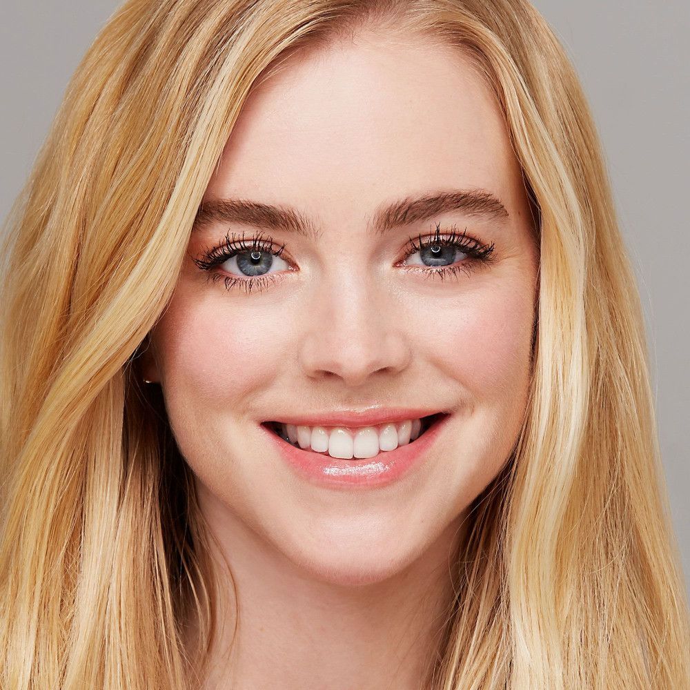 Portrait d'une femme aux cheveux blonds et aux cils maquillés. Elle sourit.