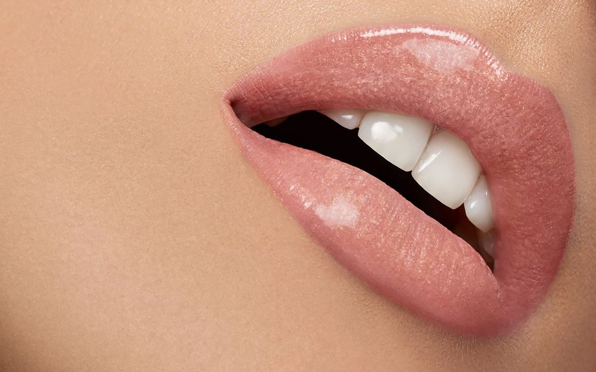 Gros plan sur des lèvres maquillées avec du rouge à lèvres rose. Bouche ouverte, dents visibles. Peau en arrière-plan.