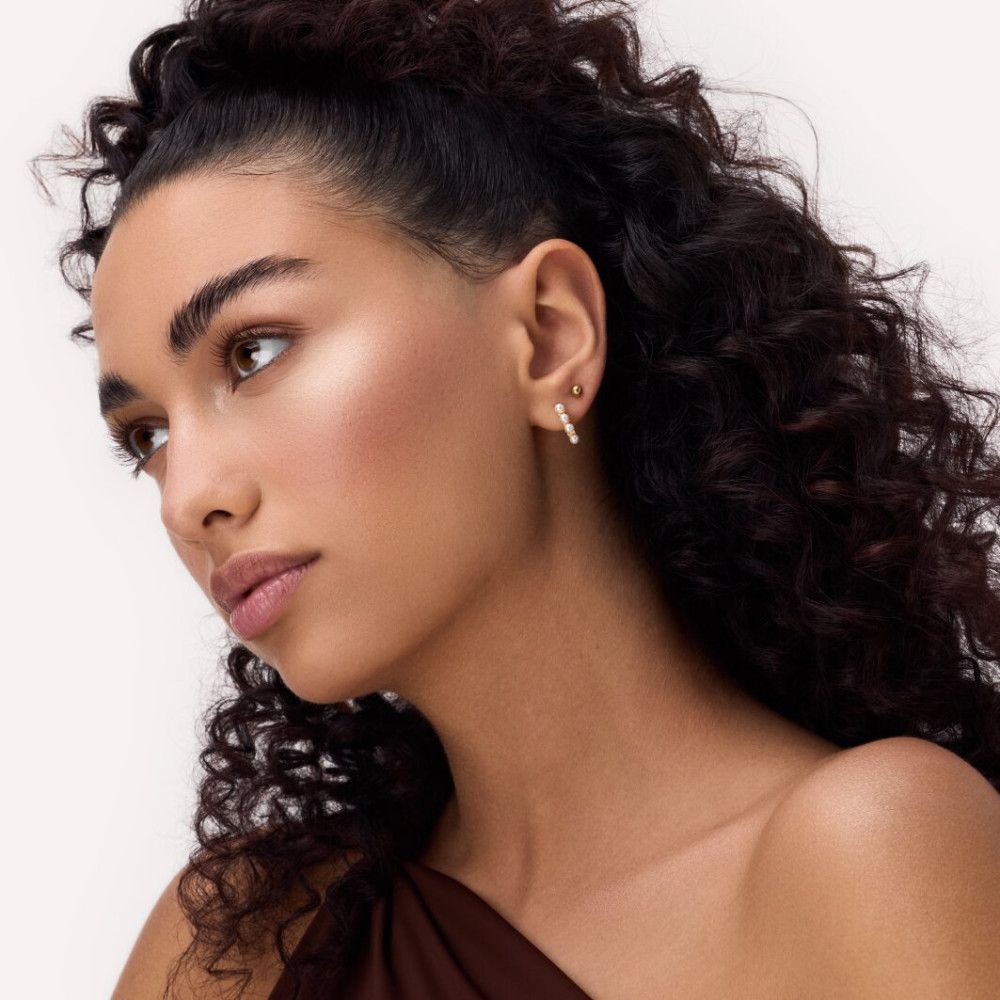 Portrait d'une femme avec des boucles et du surligneur appliqué. Teint et boucles d'oreilles visibles.