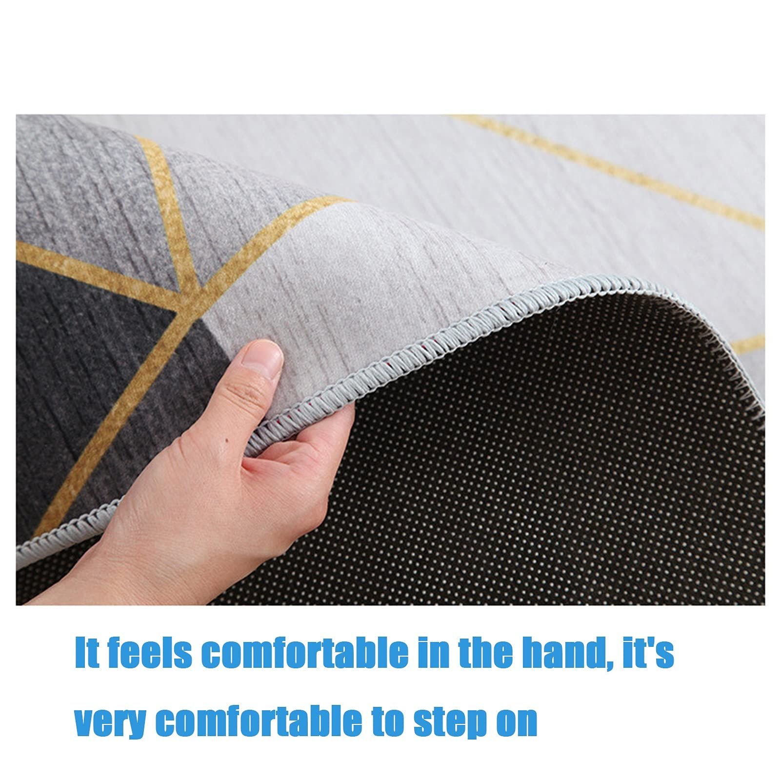 Tapis à motifs géométriques. Triangles gris, jaunes et noirs. Main tenant le bord. Texte : Agréable au toucher, très agréable à fouler.