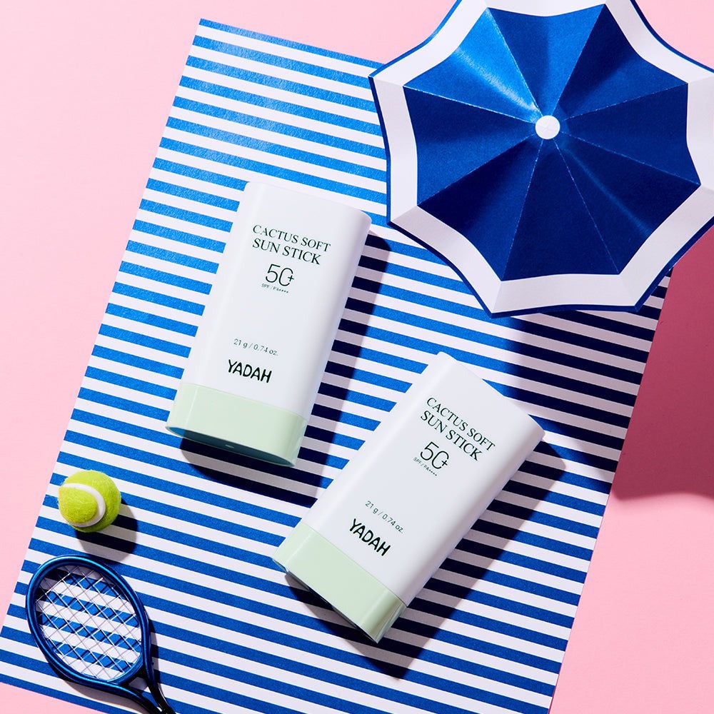 Twee witte YADAH Cactus Soft Sun Stick 50g zonnebrandsticks met lichtgroene onderkant op een blauw-wit gestreept handdoek.