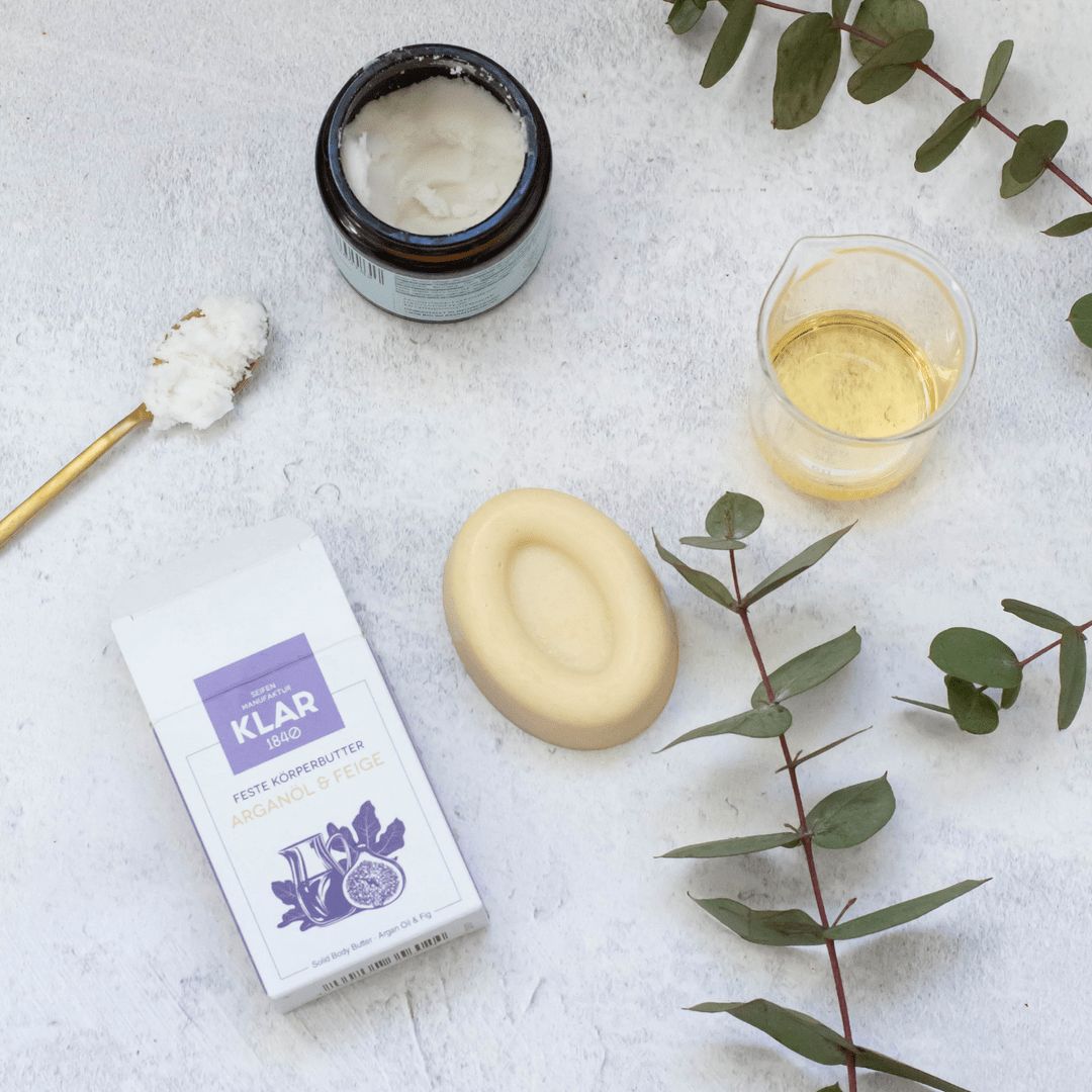 Bovenaanzicht. Vaste body butter, verpakking, crème in glas, olie in beker, lepel, eucalyptus takken. Productnaam: Arganolie & Vijg.