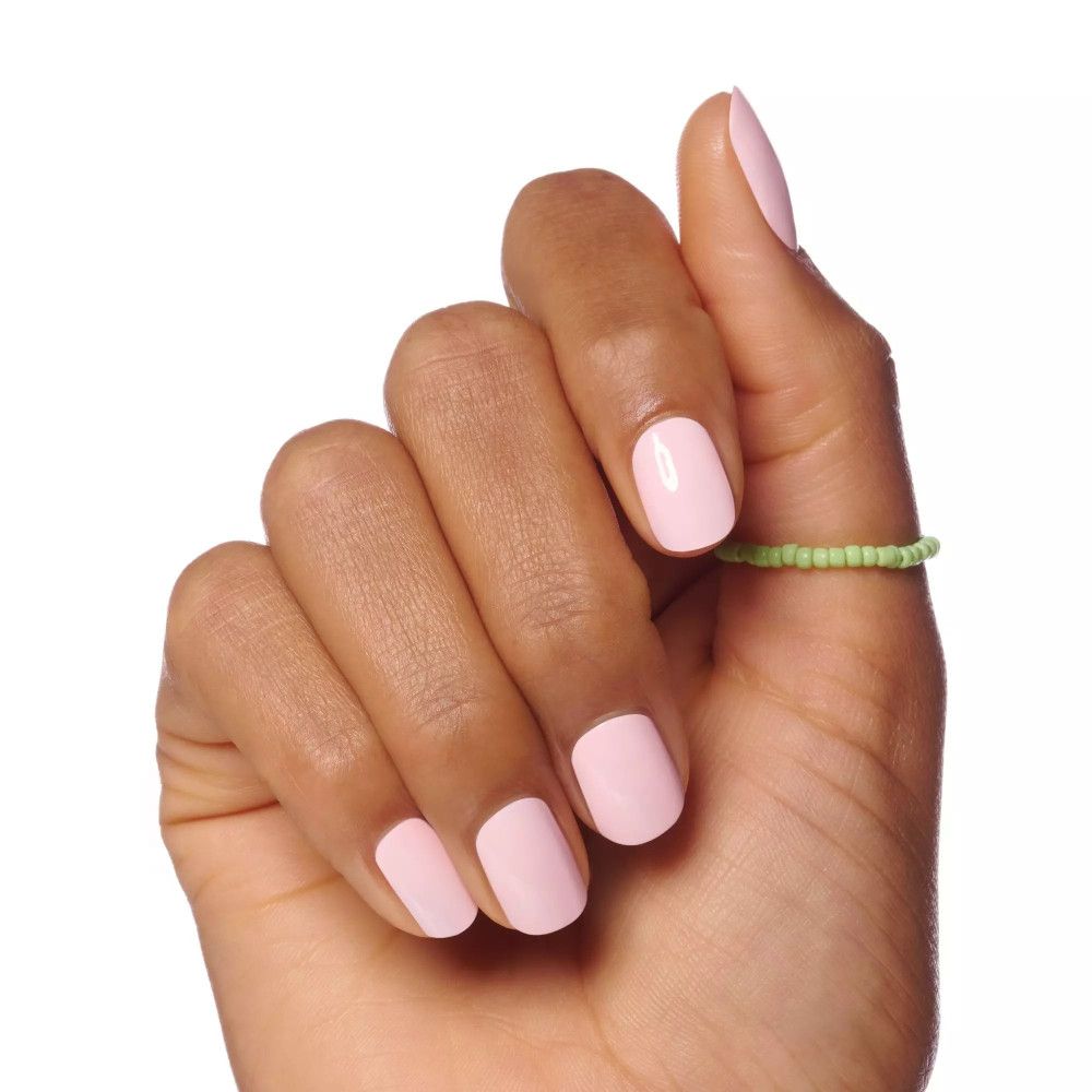 Main avec ongles vernis en rose. Une bague verte sur le doigt.