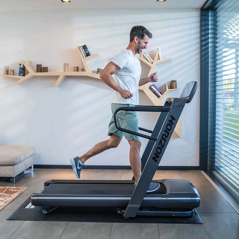Homme courant sur un tapis de course. Tapis de course avec affichage numérique. Marque : HORIZON. Modèle : Omega Z. Environnement : salon.