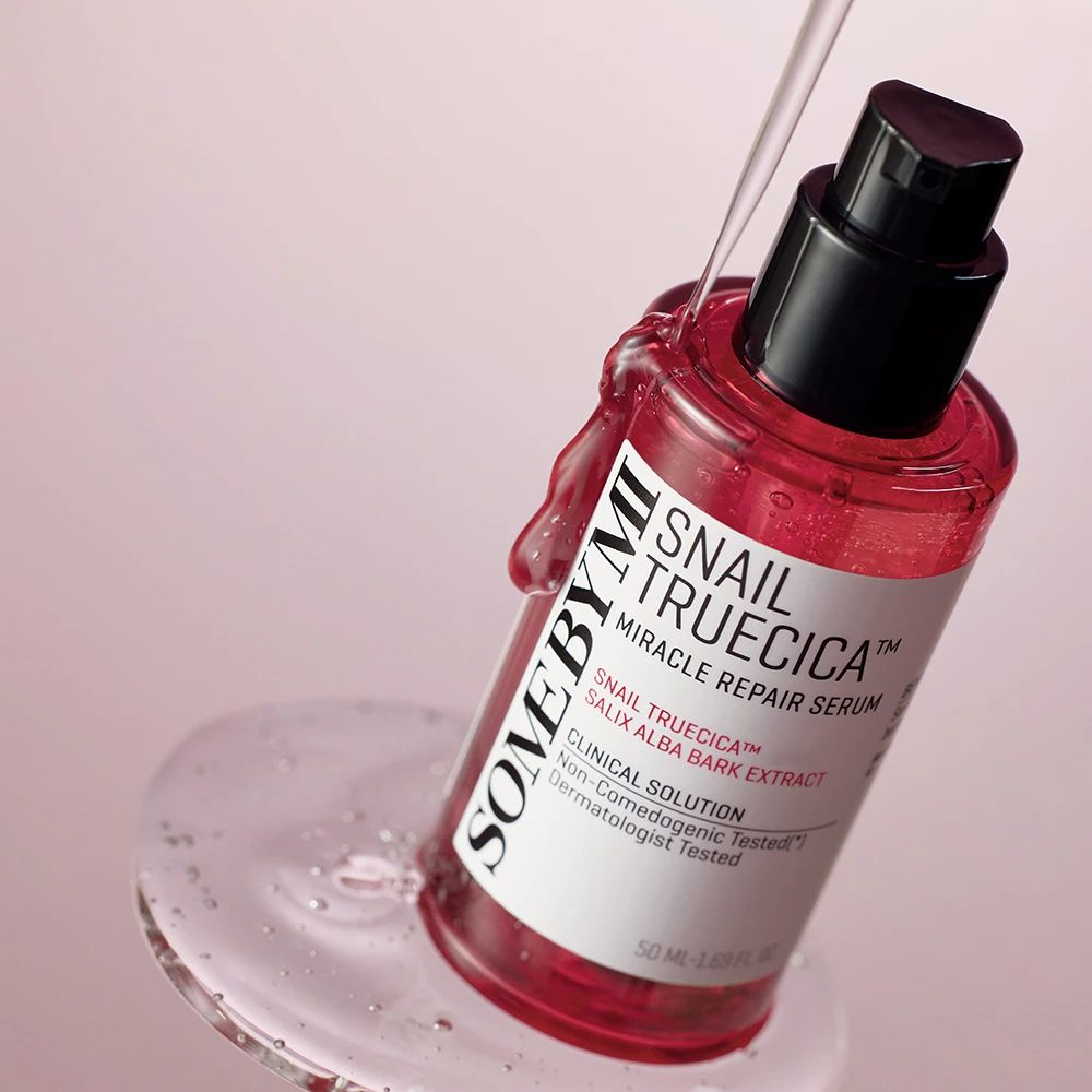 Rode serumfles met zwarte pomp. Productnaam en ingrediënten op etiket. Vloeistof druppelt uit fles.