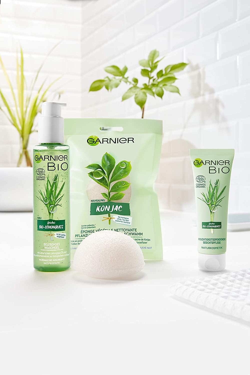 Trois produits: gel lavant, éponge Konjac, hydratant. Inscription Garnier Bio. Fond: mur carrelé blanc.