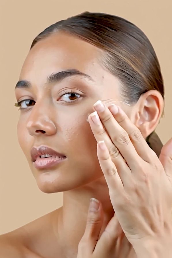 Femme appliquant un produit sur son visage. Peau claire, cheveux bruns. Produit appliqué.