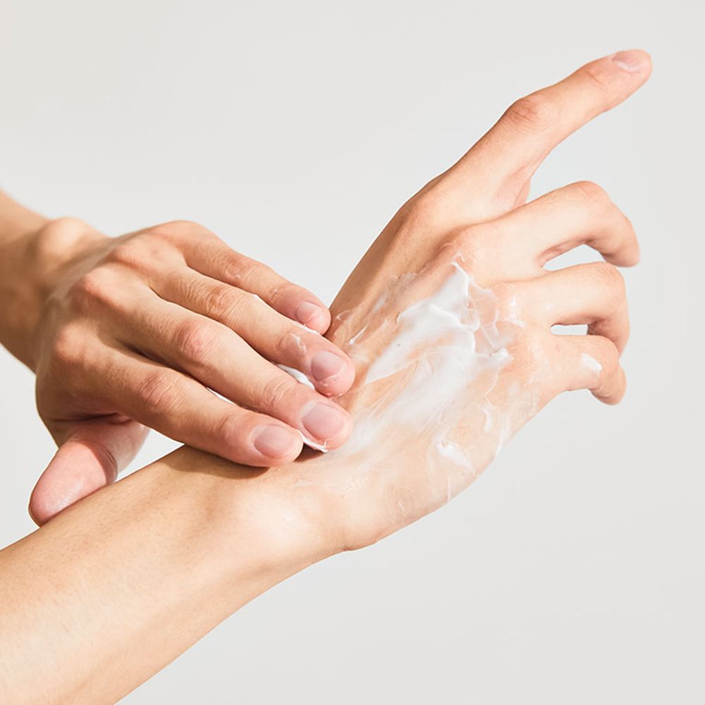 Mains appliquant une crème sur la paume. La crème est blanche et la peau légèrement rouge.