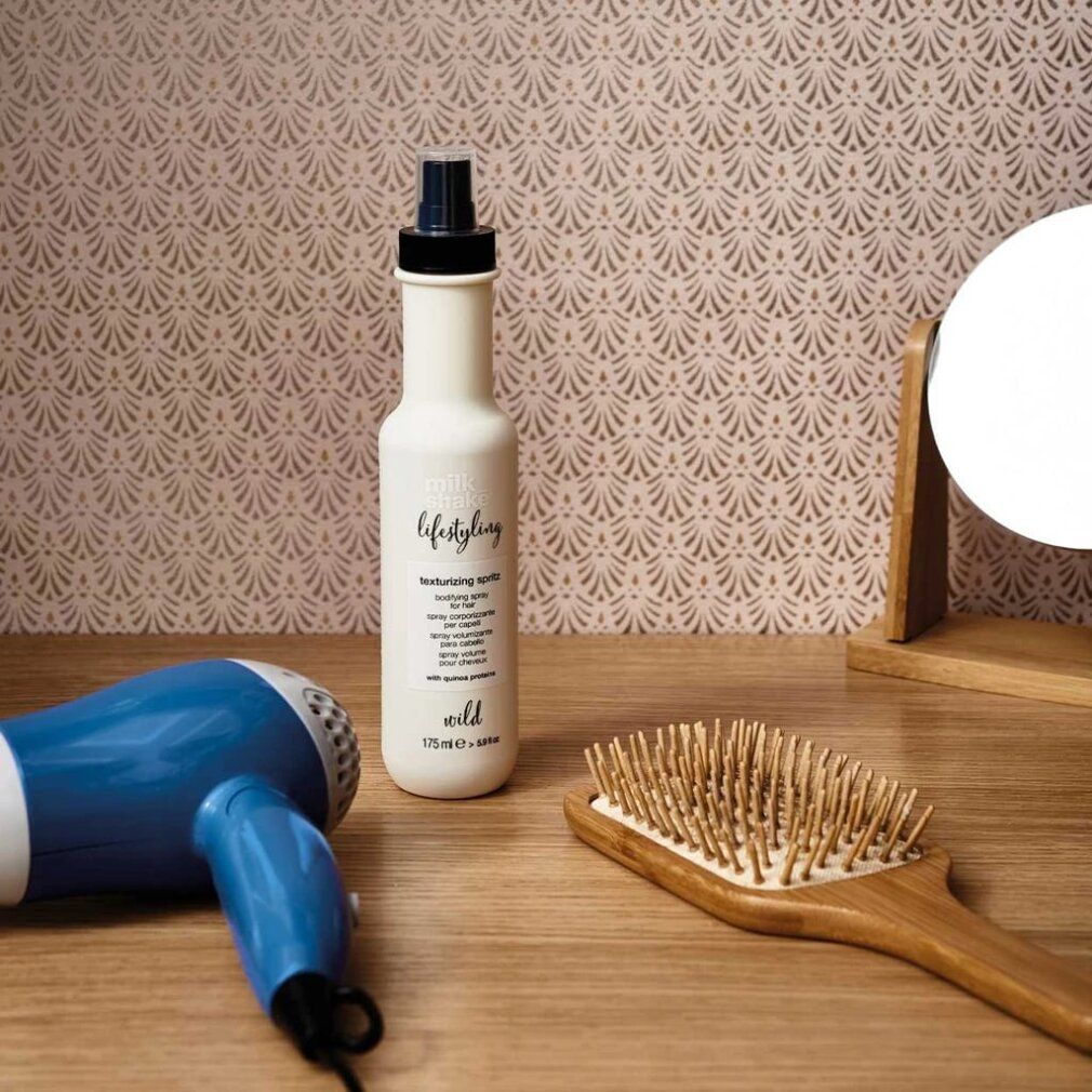 Flacon beige avec vaporisateur noir, à côté d'un sèche-cheveux, d'une brosse et d'un miroir sur une surface en bois.