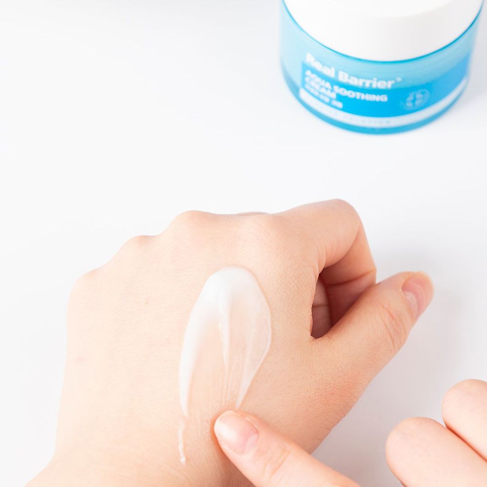 Main avec crème appliquée. La crème est blanche et brillante. Un doigt touche la crème.