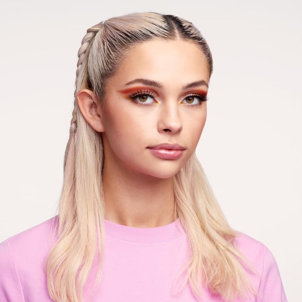 Portrait d'une jeune femme avec des tresses blondes et du maquillage. Elle porte un haut rose.