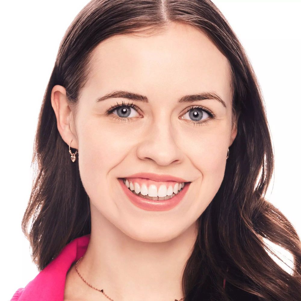 Portret van een lachende vrouw met lang bruin haar. Ze draagt oorbellen en een ketting.