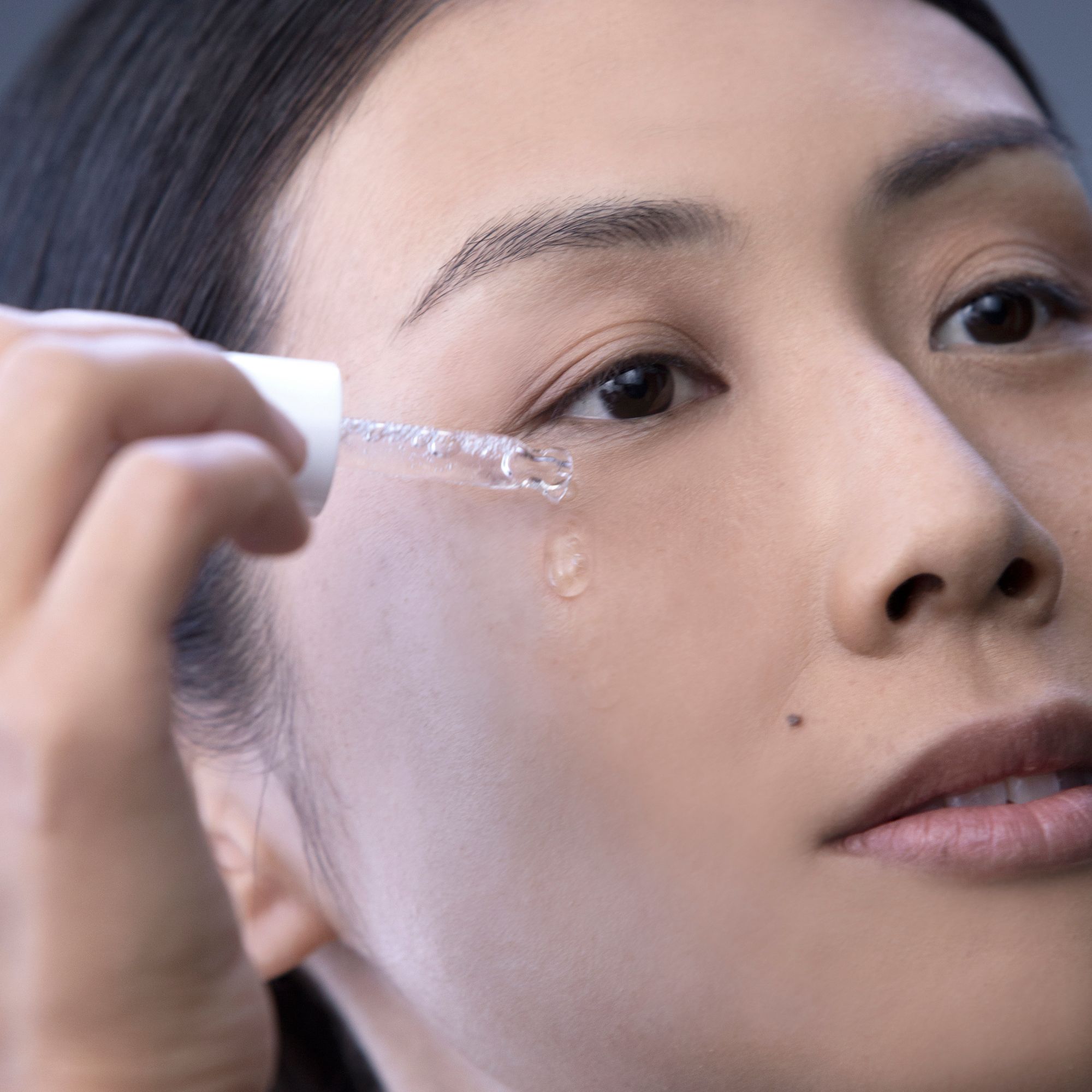 Een vrouw brengt Alkemy Pure Collagen serum aan bij haar oog met een druppelaar.