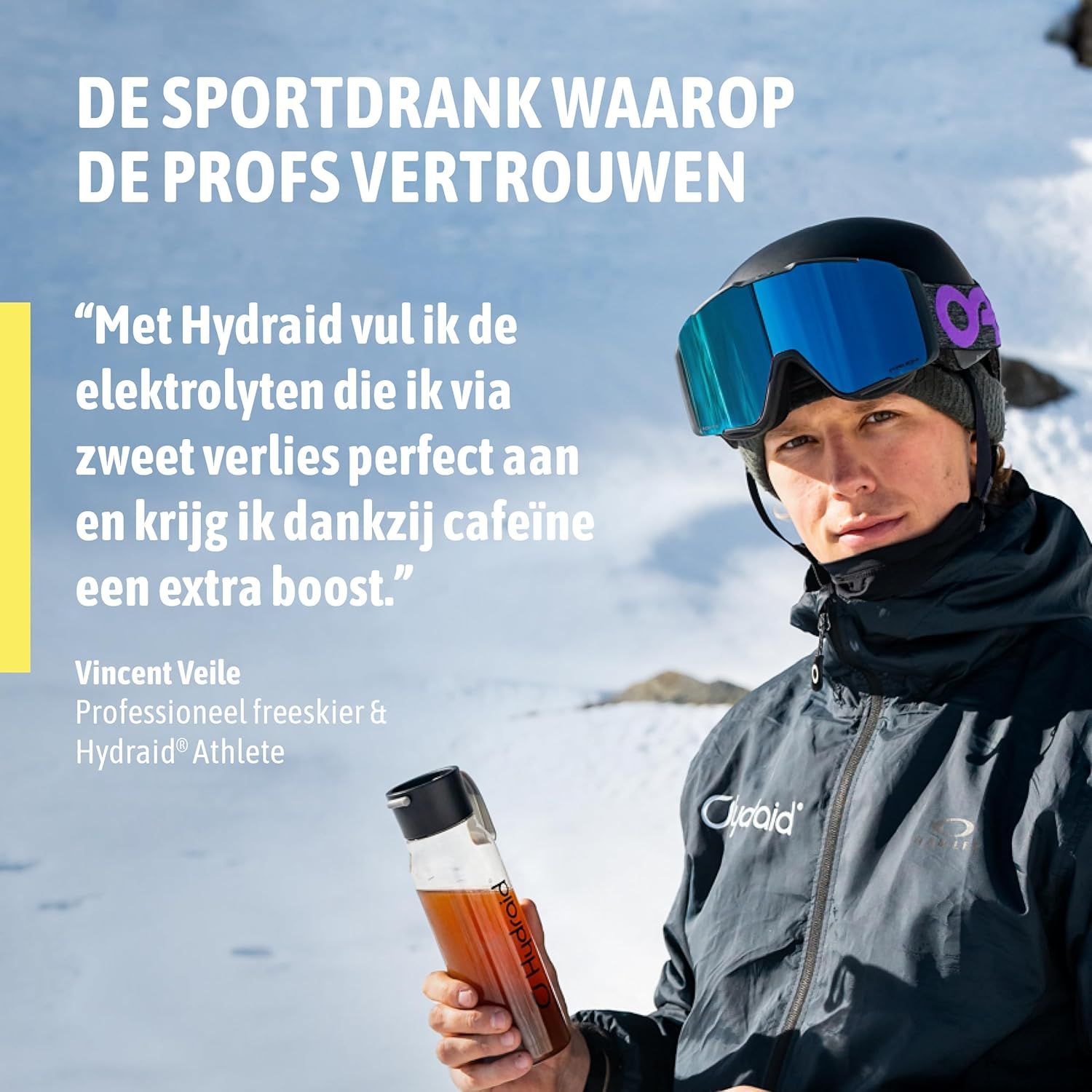 Een man in skikleding houdt een doorzichtige drinkfles met bruine vloeistof vast. Hij draagt een skibril en helm.