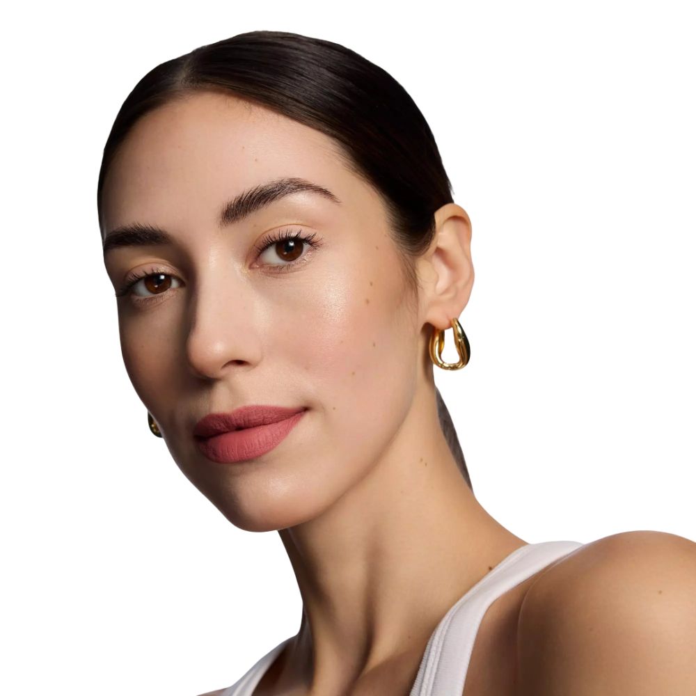 Portrait d'une femme portant du rouge à lèvres rose. Elle porte des boucles d'oreilles dorées et un haut blanc. Ses cheveux sont attachés.