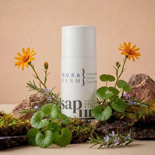 Witte fles met pompdosering, opschrift 'NORADERM' en 'sapura', omringd door mos en bloemen.