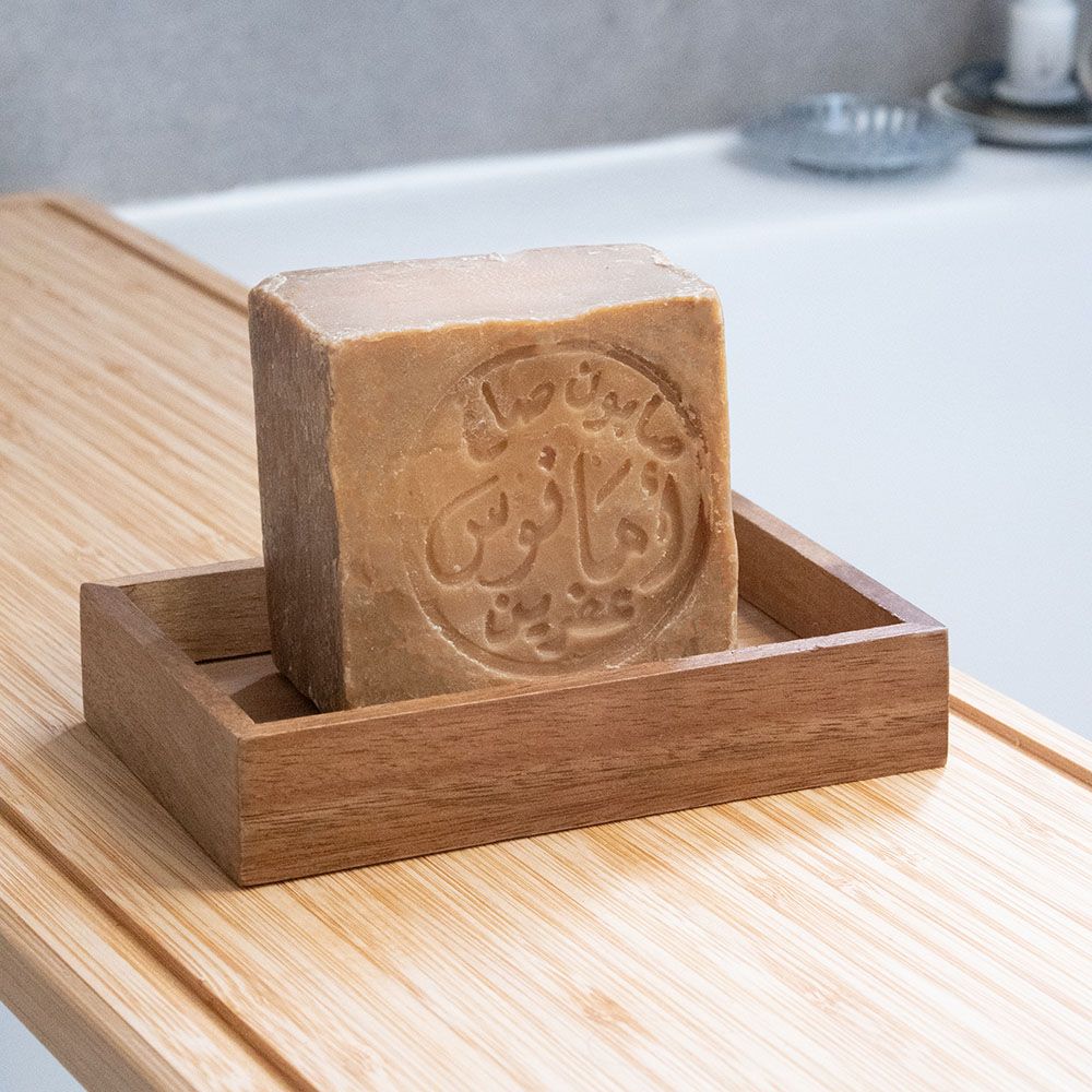 Un savon carré, inscription arabe, dans un porte-savon en bois. Sur planche de bois.
