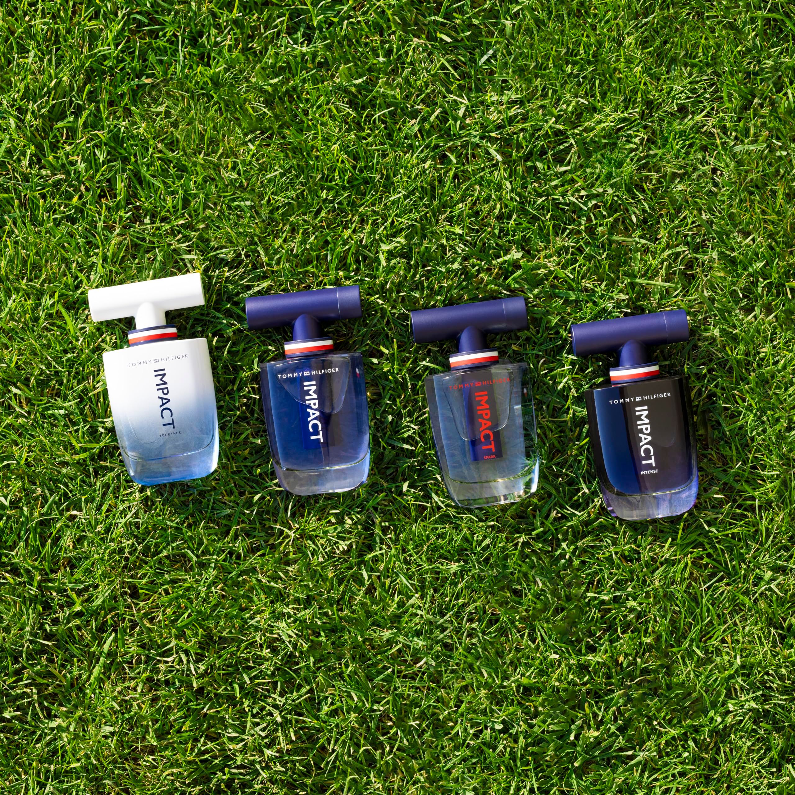 Vier flacons Tommy Hilfiger Impact Together Eau de Toilette op gras. Blauwe en witte flacons. Tekst: IMPACT.