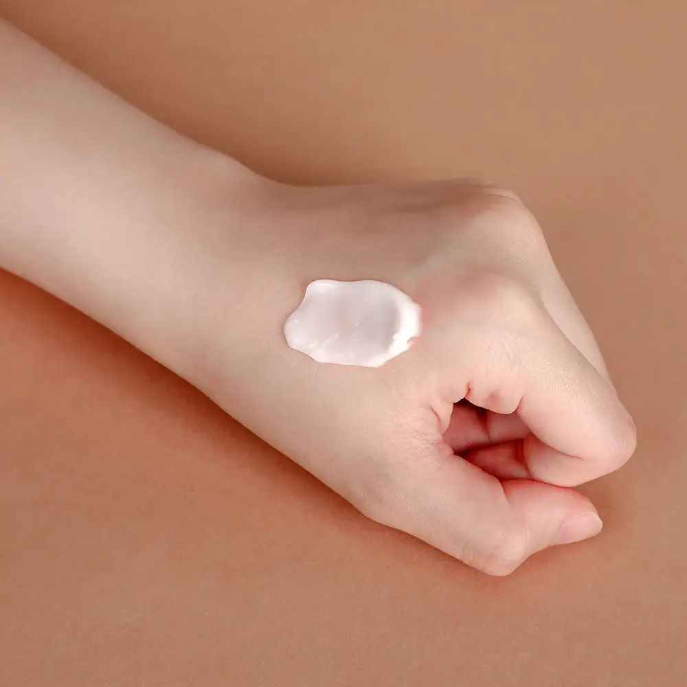 Hand met crème op bruine achtergrond. Crèmeklont op de handpalm.