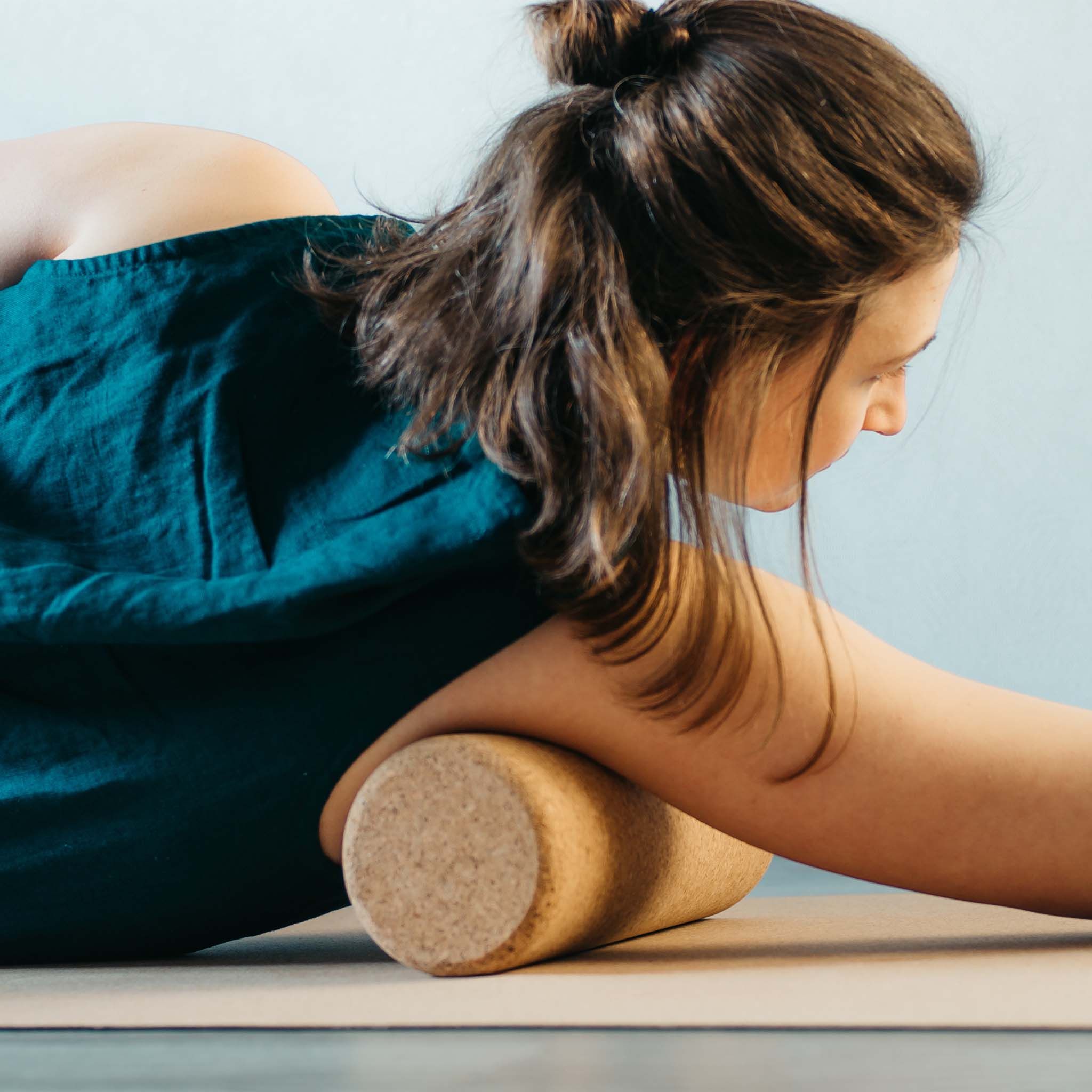 Personne utilisant un rouleau de fascia en liège. Rouleau marron sous le bras sur un tapis.