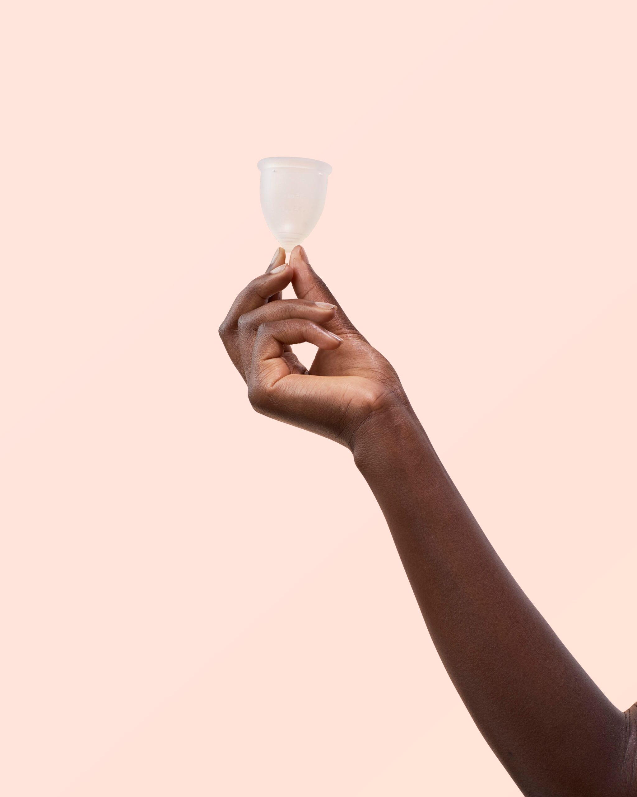 Main tenant une coupe menstruelle en silicone transparent. Fond rose.