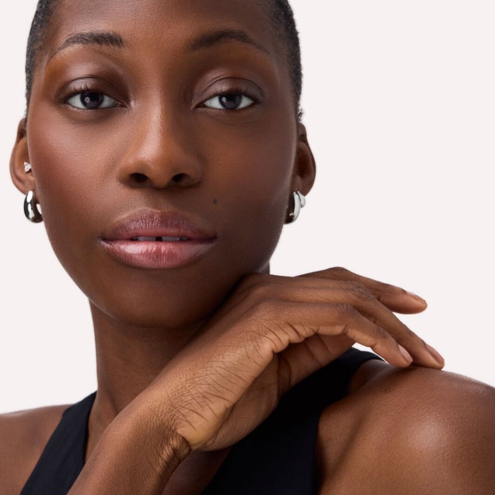 Portrait d'une femme à la peau foncée. Elle porte des créoles argentées et a les lèvres brillantes.
