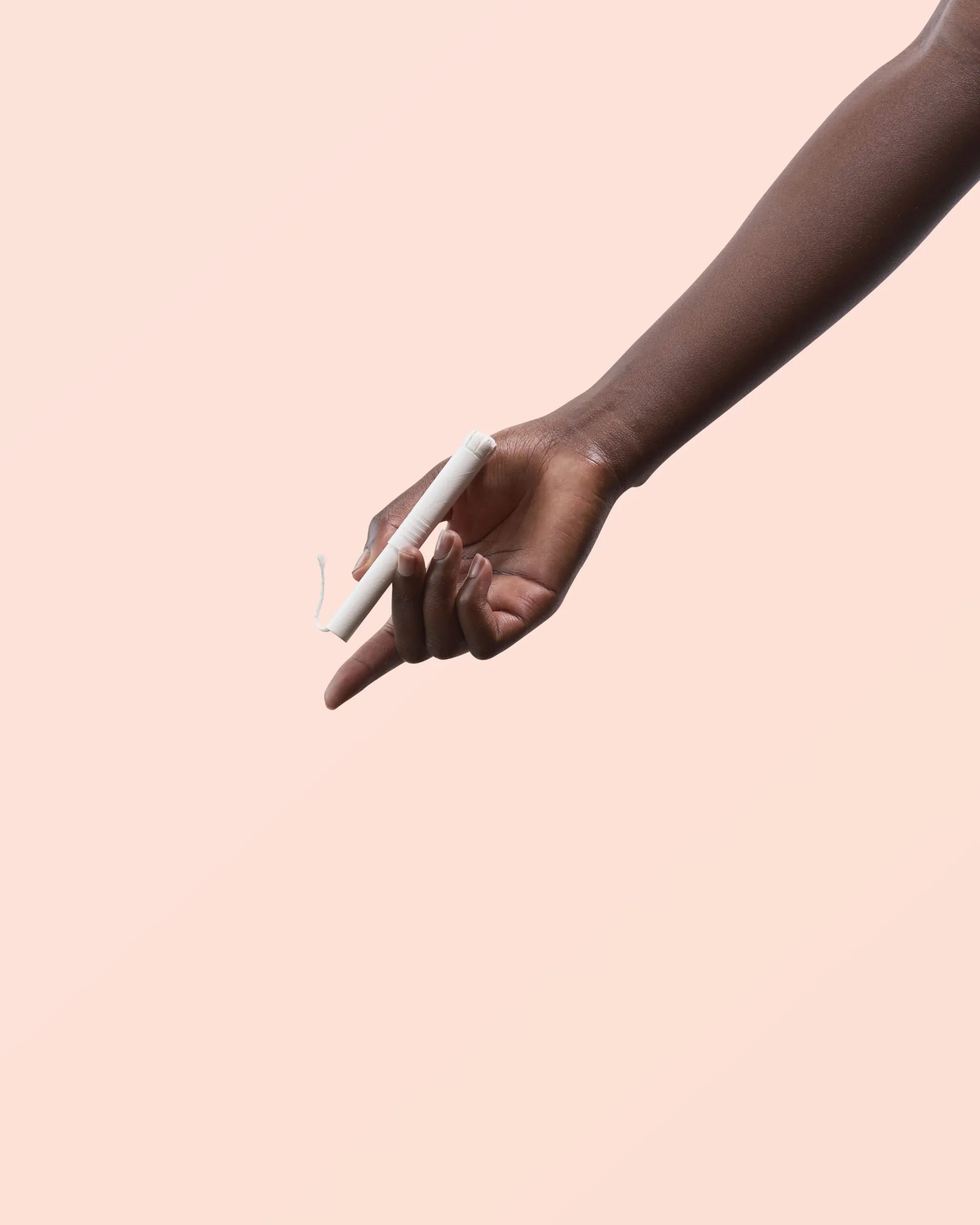 Witte tampon met applicator, vastgehouden door een hand. Op roze achtergrond.
