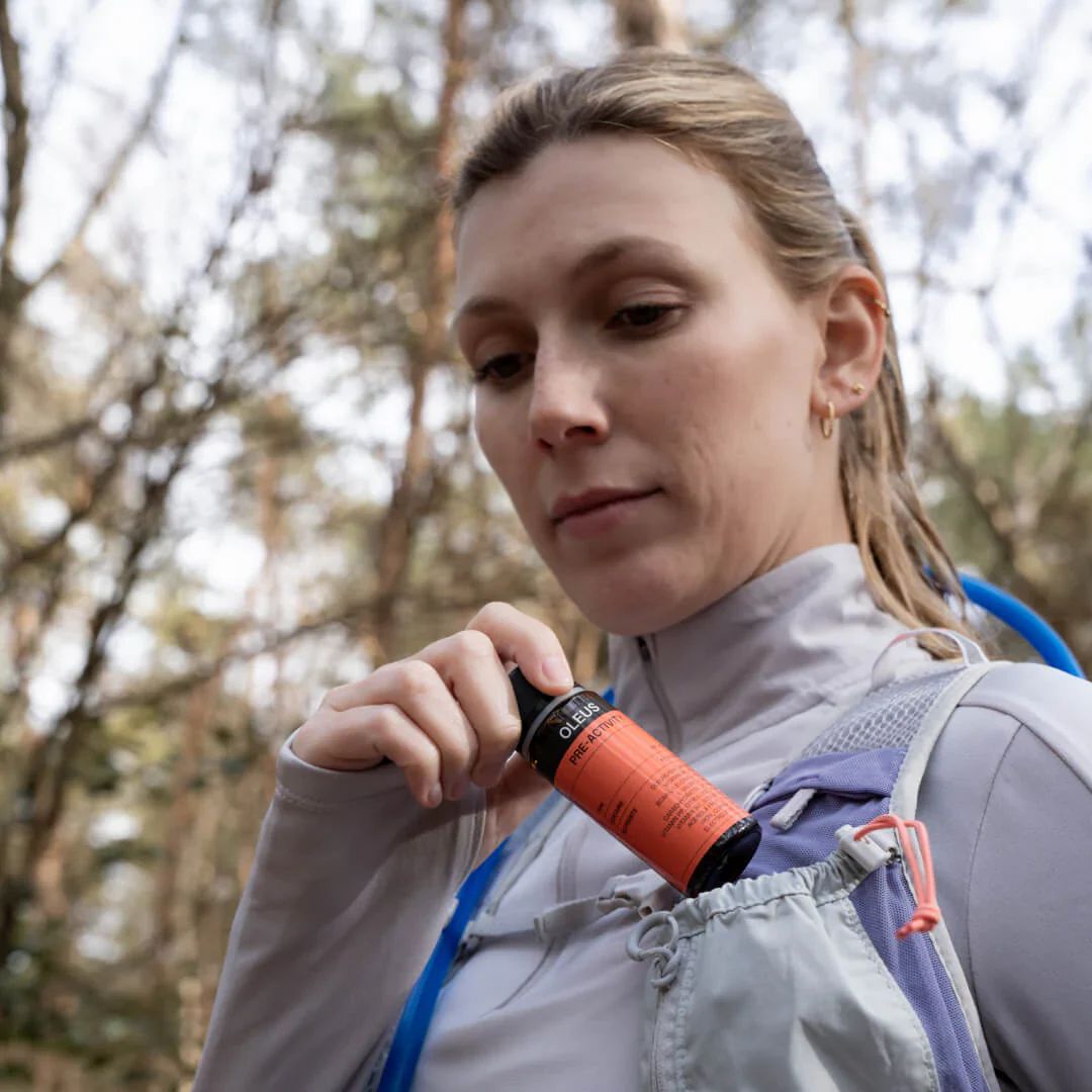 Vrouw met flesje in rugzaktas. Flesje met label. OLEUS-logo en productinfo zichtbaar.