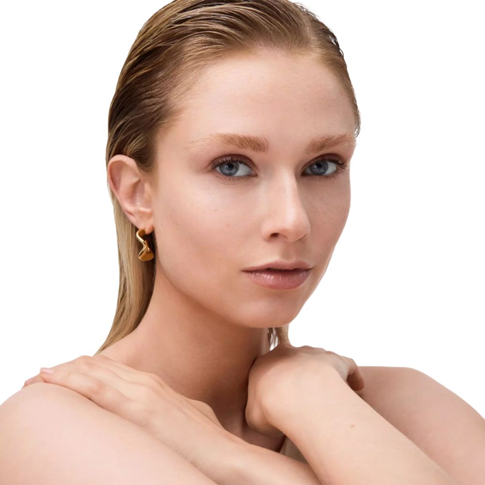 Portrait d'une femme aux cheveux blonds et boucles d'oreilles dorées. Elle regarde la caméra.