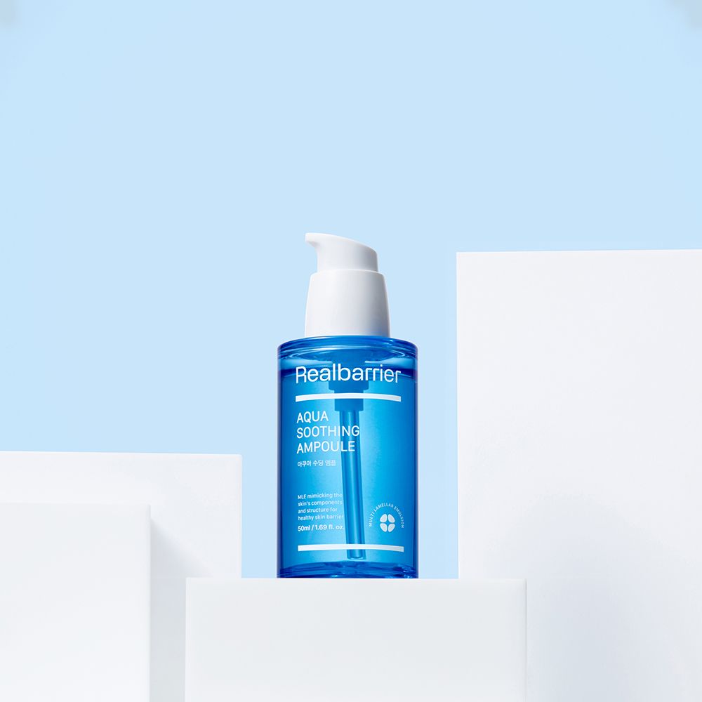 Blauw serum met witte pomp op wit voetstuk. Opschrift: Realbarrier Aqua Soothing Ampoule.