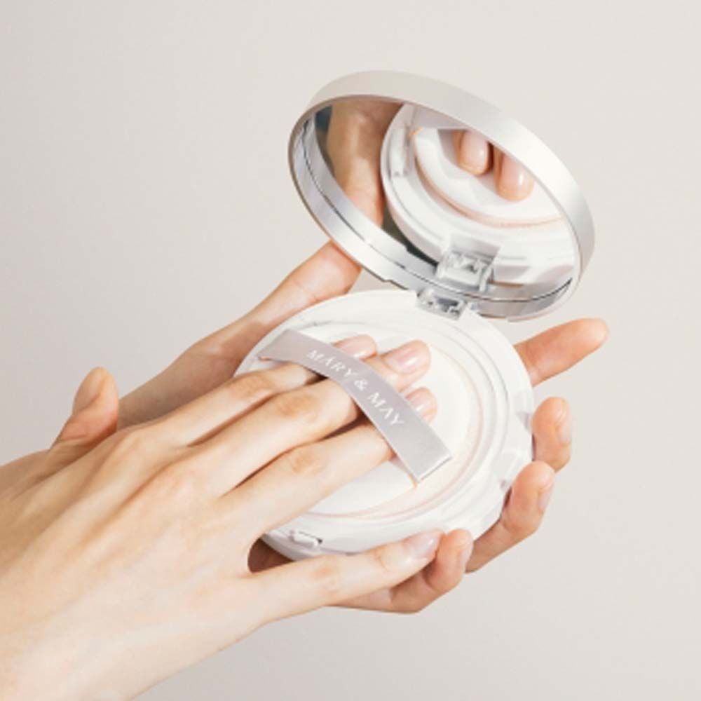 Handen houden een open cushion poederdispenser met spiegel en applicator vast.