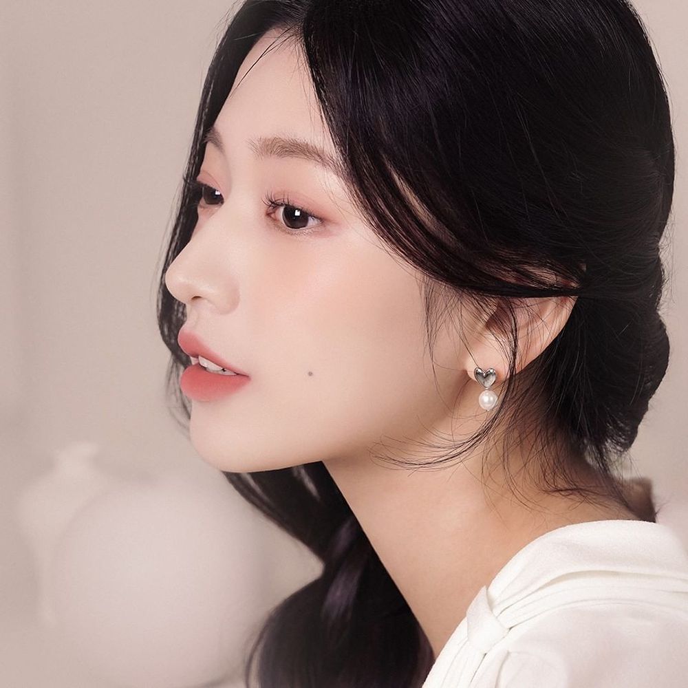 Portrait d'une femme de profil. Elle porte un haut blanc. Ses cheveux sont sombres et attachés. Elle porte une boucle d'oreille.