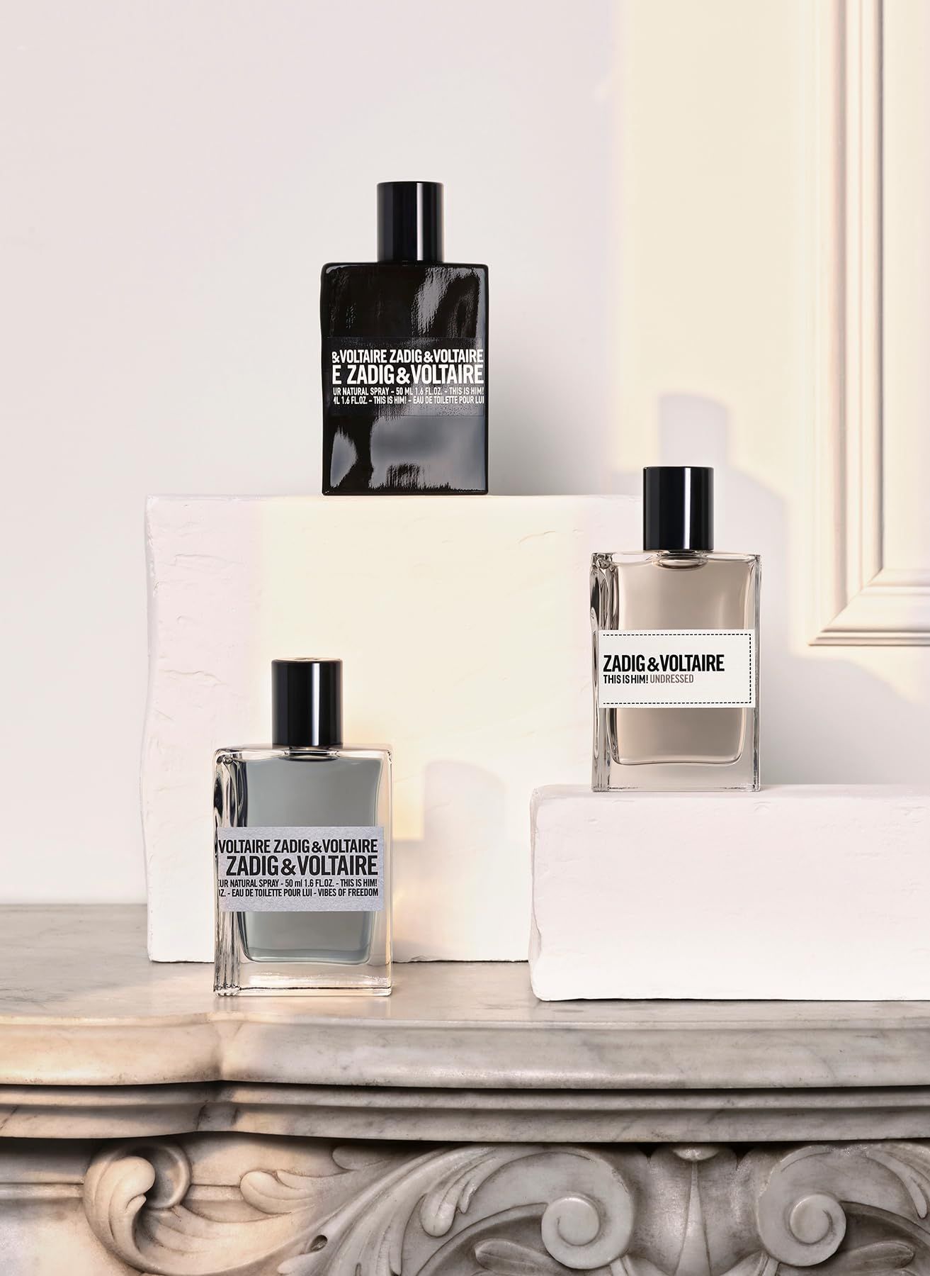 Drie Zadig & Voltaire flacons. Zwarte, grijze en heldere flacon. Op witte blokken. Zwarte doppen.