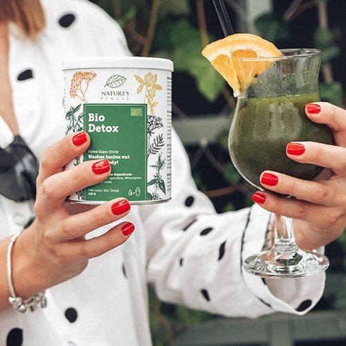 Personne tenant une boîte et un verre de boisson verte. Boîte: Bio Detox, Herbal Super Drink. Avec label bio. Verre avec tranche d'orange.