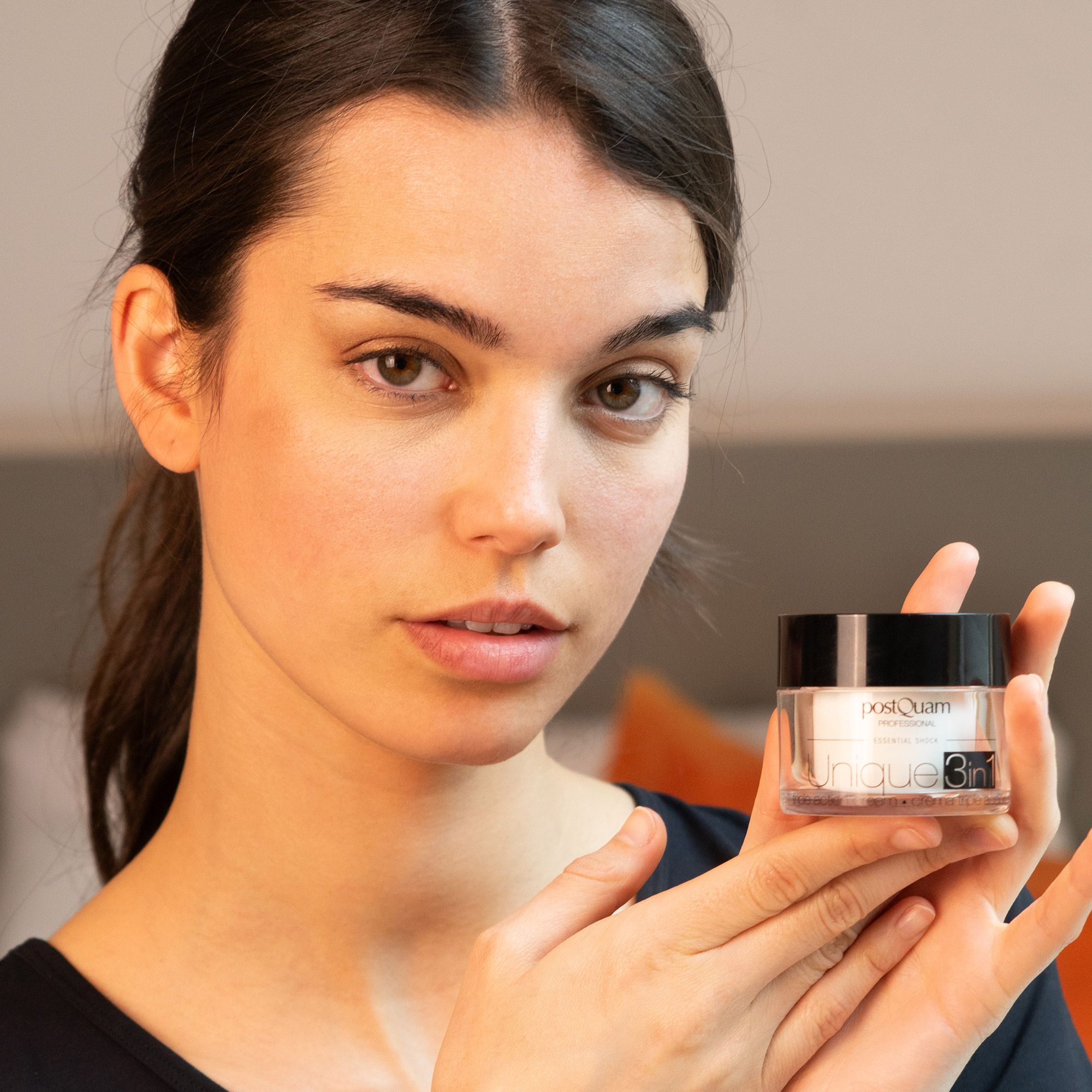 Femme tenant un pot de crème avec couvercle noir. Inscription : Postquam Professional, Unique 3in1. Crème triple action.