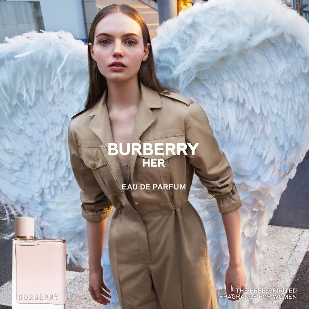 Femme avec des ailes et flacon Burberry Her Eau de Parfum. Inscription : Burberry Her Eau de Parfum.