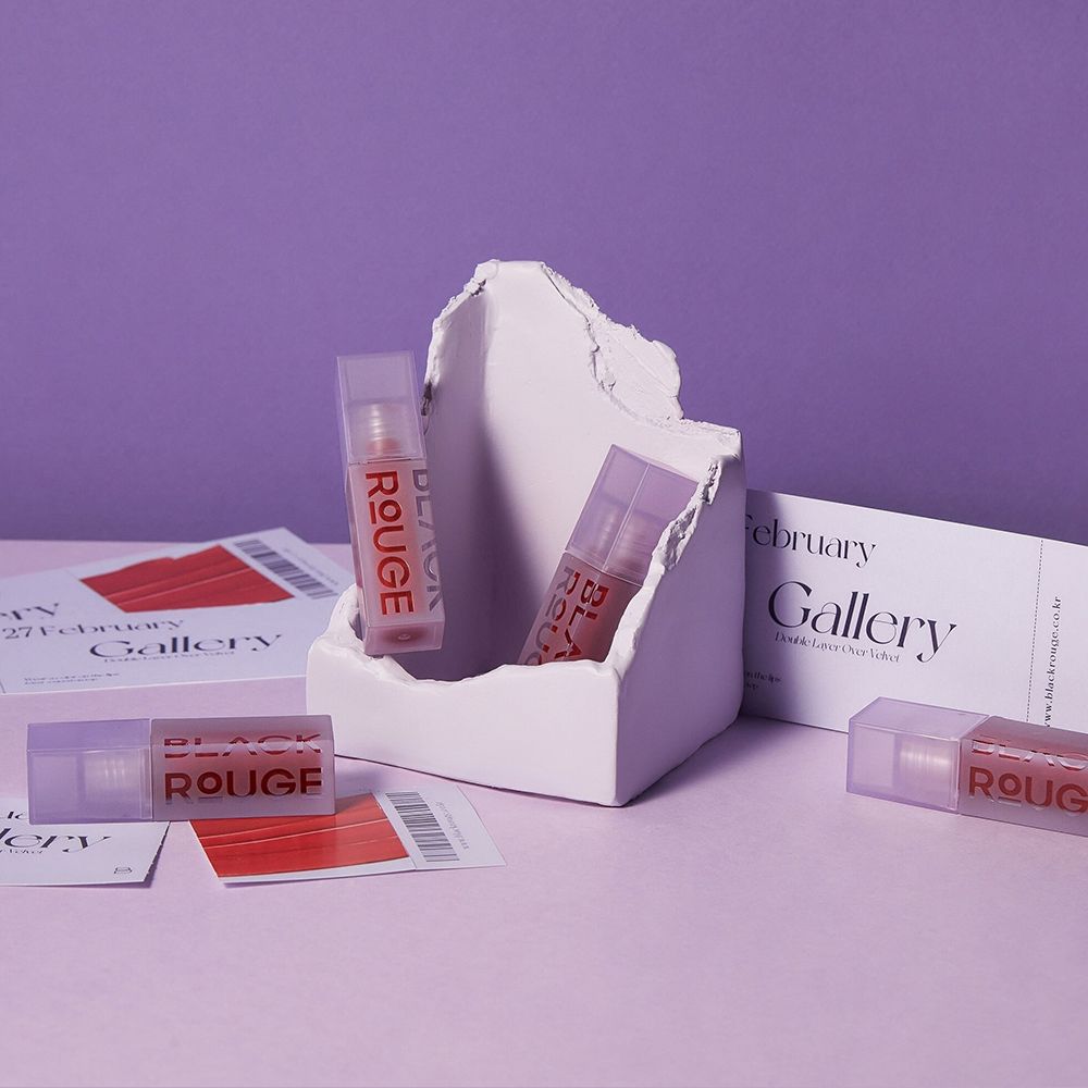 Verschillende lipgloss tubes met paarse doppen. "BLACK ROUGE" staat op de tubes. Op een paarse achtergrond.