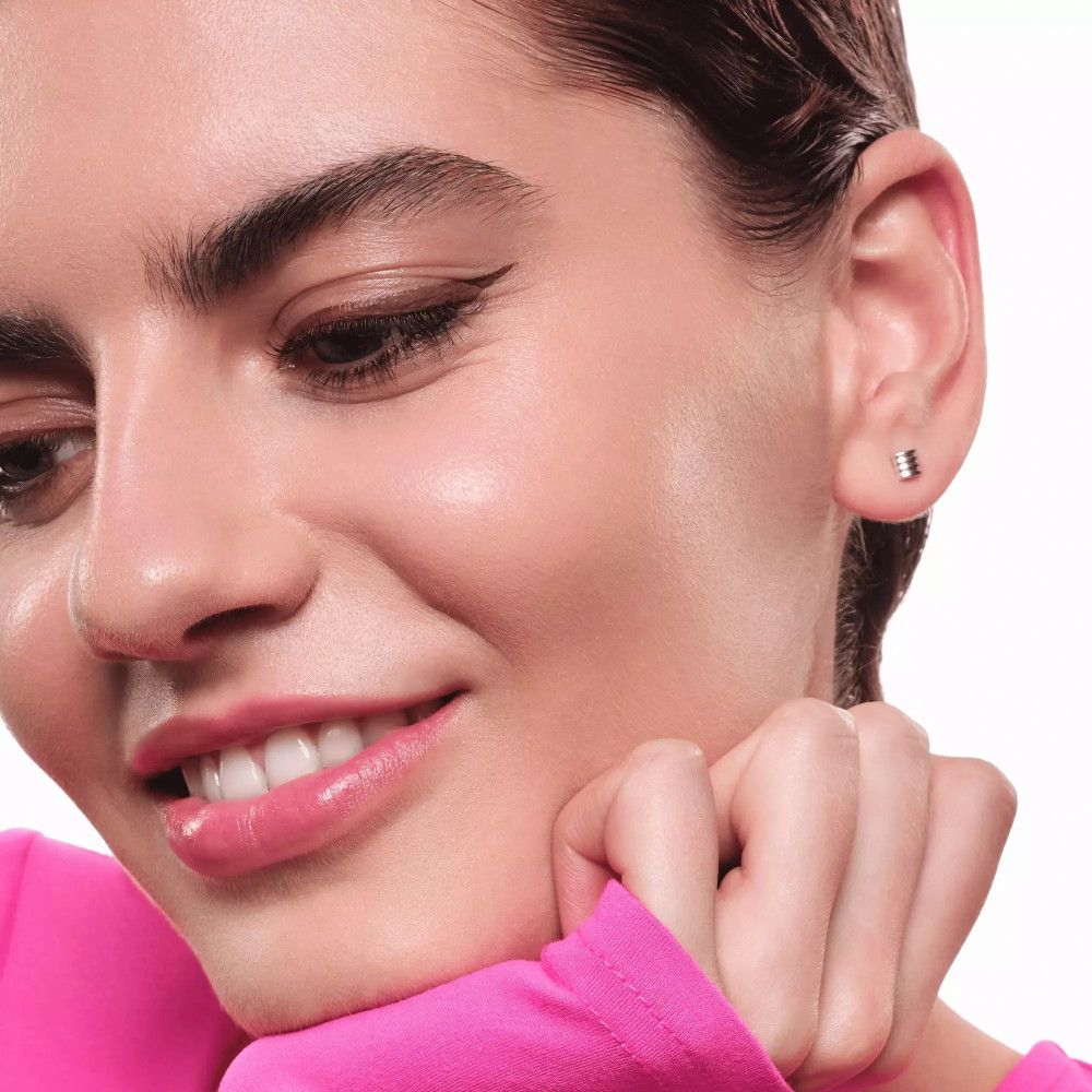 Portrait d'une femme souriante avec de l'eyeliner. Elle porte un haut rose.