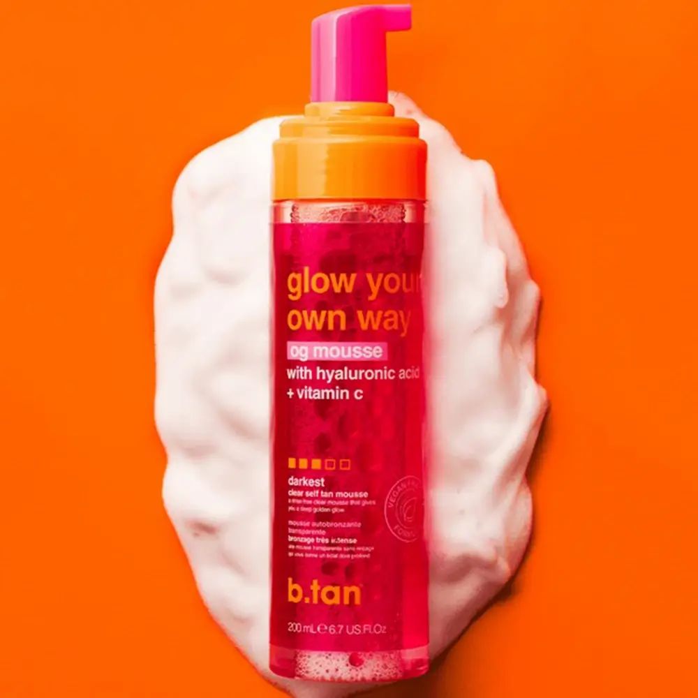 Flacon rose avec pompe sur mousse blanche. Inscription : glow your own way, the og mousse, avec acide hyaluronique + vitamine C. Marque : b.tan.