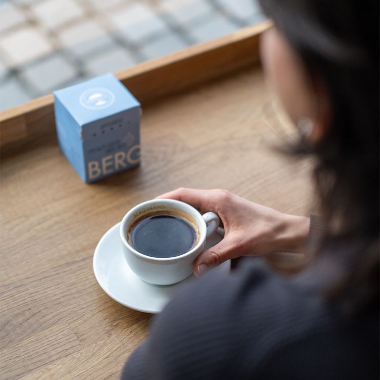 Personne boit du café dans une tasse blanche avec soucoupe. Boîte BERGBRAND bleue en arrière-plan.