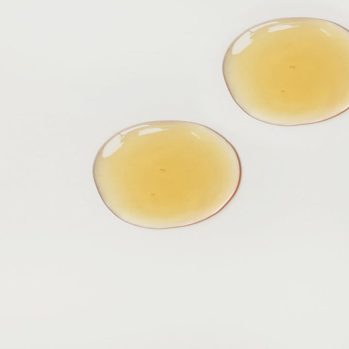 Deux gouttes de liquide jaunâtre sur fond blanc. Forme ronde avec une légère brillance.
