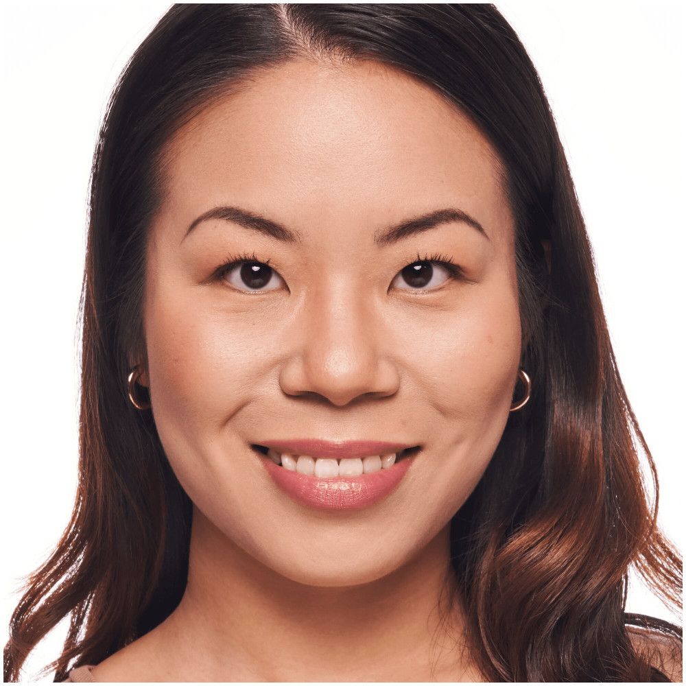 Portrait d'une femme avec fond de teint. Teint naturel, cheveux foncés, boucles d'oreilles dorées. Fond blanc.