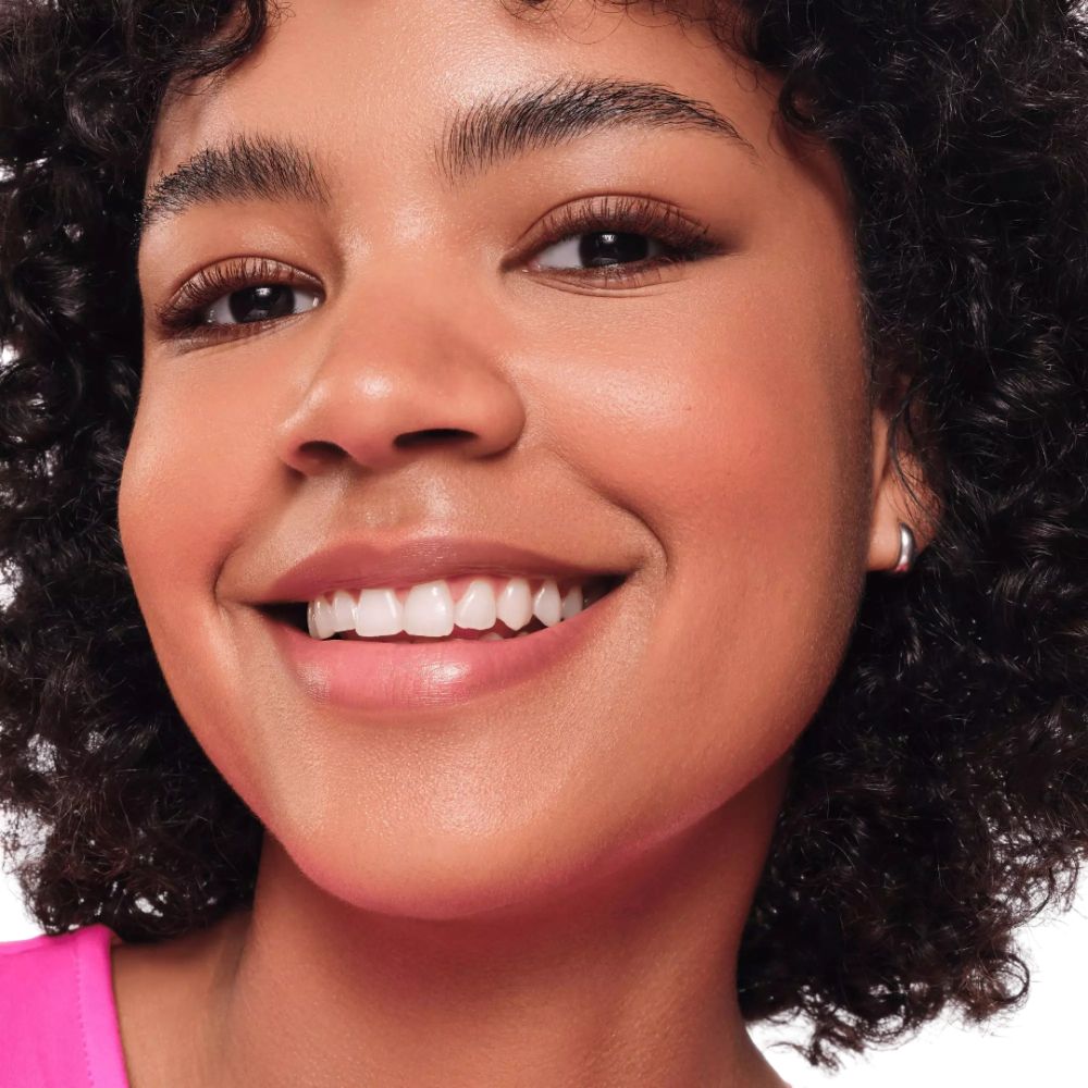 Gros plan d'un visage souriant. Cheveux bouclés, boucle d'oreille. Haut rose.