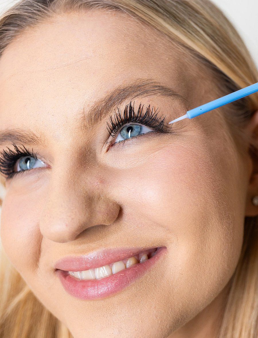Une femme applique le sérum pour cils LUXE LASH sur ses cils supérieurs avec un applicateur fin.