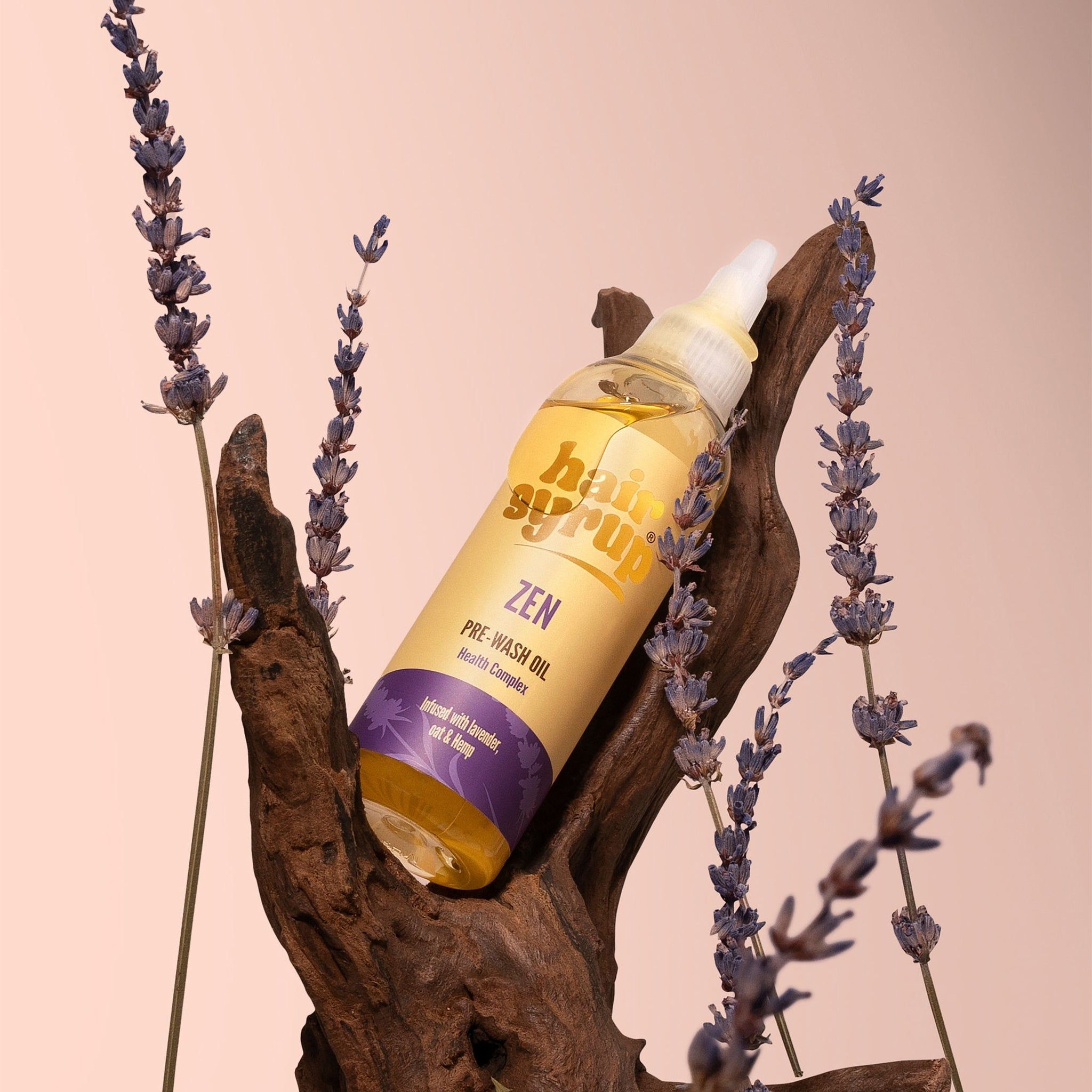 Un flacon de liquide jaune avec étiquette. Le flacon est posé sur un morceau de bois, entouré de lavande.