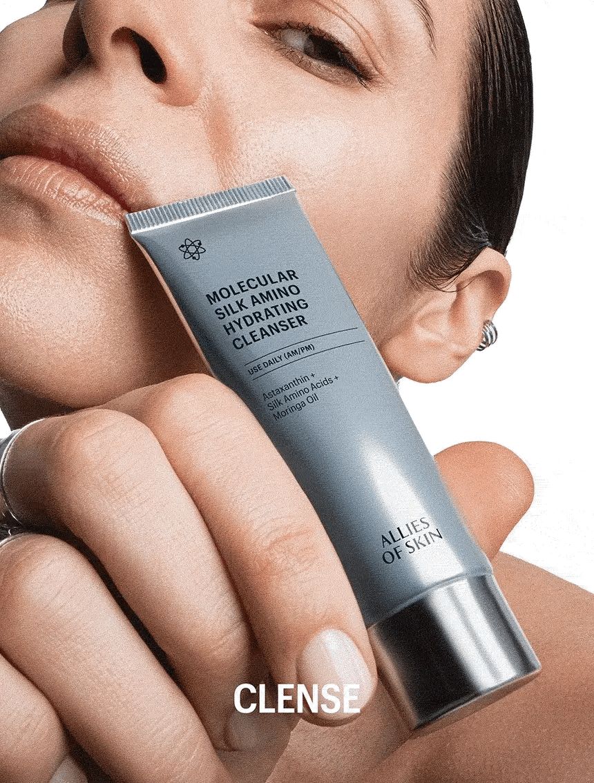 Personne tenant un tube. Inscription: Molecular Silk Amino Hydrating Cleanser. Marque: ALLIES OF SKIN. Texte: CLENSE.