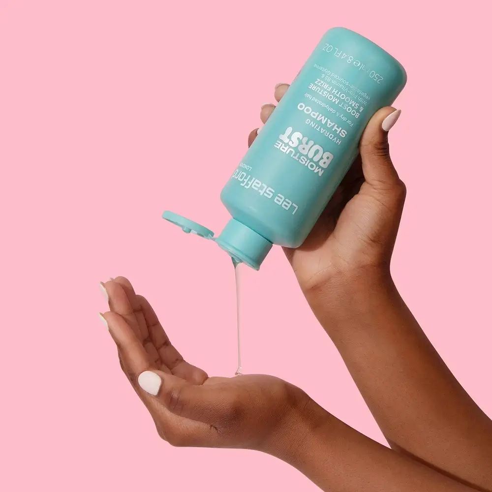 Turquoise shampoo fles wordt in de hand gegoten. Opschrift: Moisture Burst Hydrating Shampoo. Merk: Lee Stafford.