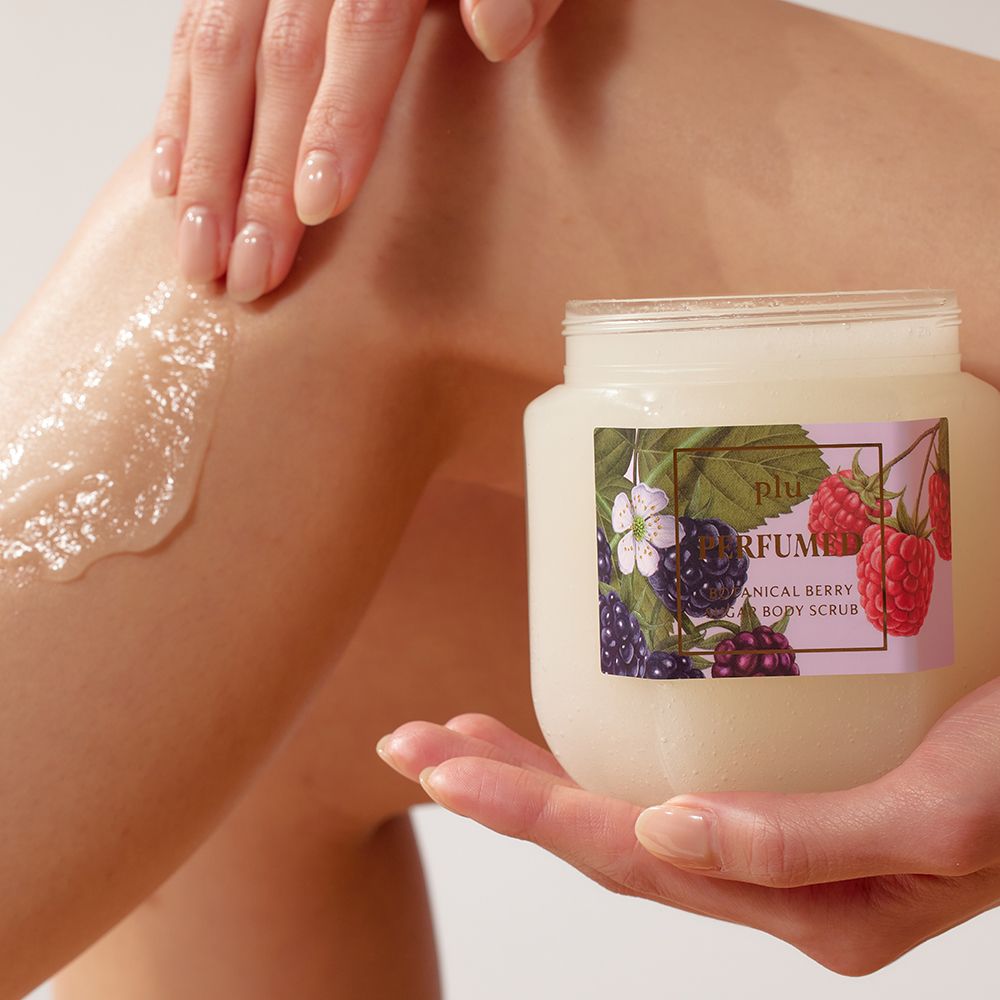 Persoon houdt een glazen pot vast. Product wordt op been aangebracht. Etiket met bessen- en bloemenillustraties. Opschrift: PERFUMED BOTANICAL BERRY.