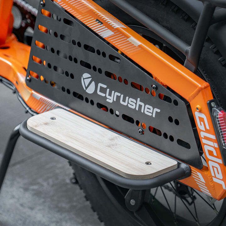 Oranje fiets met zwarte bagagedrager en houten treeplank. Cyrusher-logo zichtbaar.