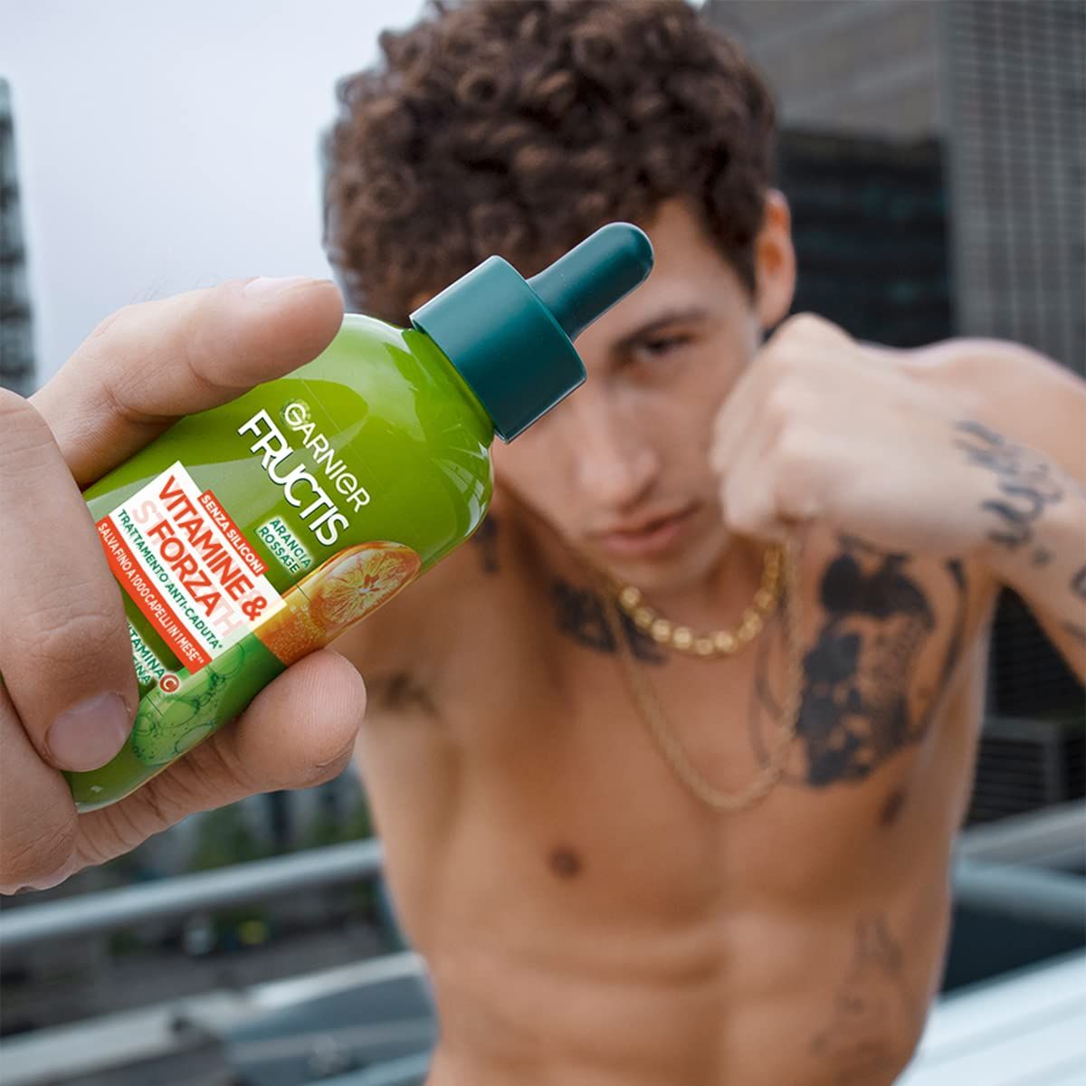 Groene fles met druppelaar, vastgehouden door een persoon. Opschrift: Garnier Fructis Vitamine & Kracht. Anti-haaruitval behandeling.